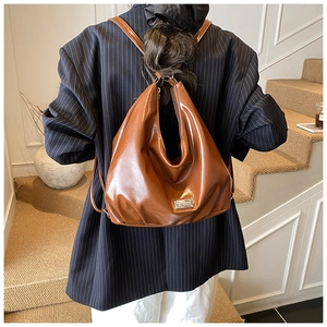 Rear view of a model wearing a brown glossy leather vintage-style backpack on shoulder