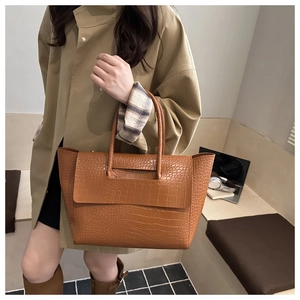 Detailed view of brown crocodile texture tote bag carried by model in beige trench coat