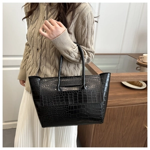 Detail of black tote bag with glossy crocodile texture pattern and slim handles for work
