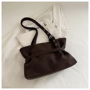 Detail of dark brown matte leather tote bag with silver buckles on white blazer