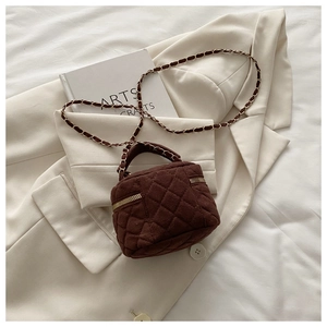 Detalle de mini bolso bandolera acolchado marrón con cadena dorada sobre un blazer