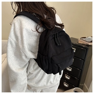Detail view of black corduroy mini backpack with drawstring side pockets on a model