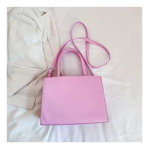 Pink minimalist crossbody bag with adjustable strap shown on a white blazer background