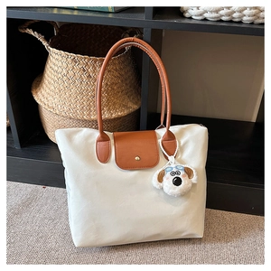 Detail of cream tote bag with brown leather flap and cute plush dog charm accessory