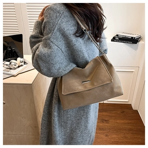 Grand sac cabas kaki avec bandoulière chaîne porté par un mannequin dans un décor chic