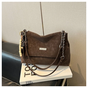 Détail d'un sac cabas en daim marron avec bandoulière chaîne et breloque en perles de bois