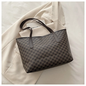 Close-up of brown tote bag with M-letter pattern and leather straps on white bedding