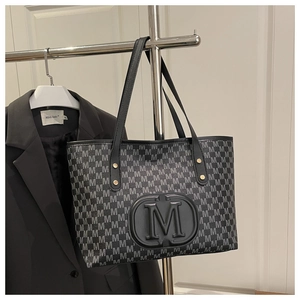 Detail of black tote bag with embossed M logo and repeated letter print pattern