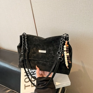 Close-up of vintage matte black shoulder bag featuring metal chain strap and wooden bead charm