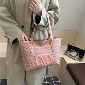 Pink tote bag with black letter print and embossed logo shown in a lifestyle setting