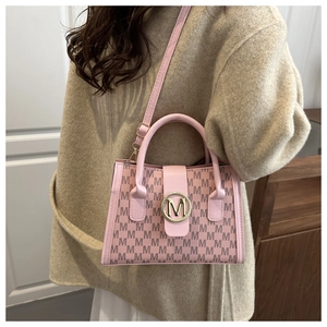 Detailed view of pink monogram crossbody bag with gold M-logo buckle worn on casual outfit