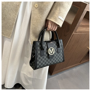 Close-up of elegant monogram fabric and golden M logo on the black leather tote bag