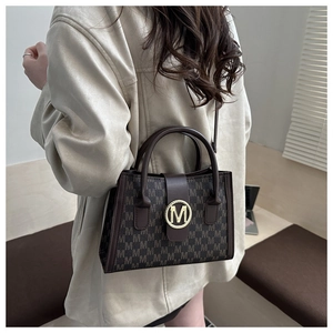 Detail of vintage brown tote bag with repeating M-letter pattern and gold logo buckle