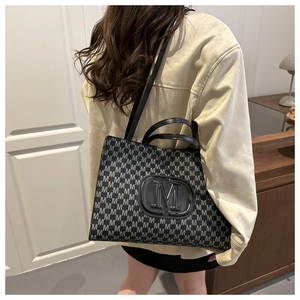 Rear view of a model wearing a large black tote bag with letter M pattern and top handles