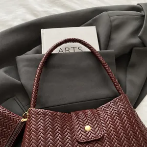 Close-up of burgundy woven leather tote bag with round metal snap button and strap