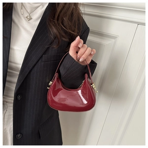 Detail of red glossy patent leather hobo bag with gold buckle on a model in suit