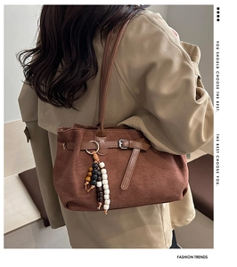 Detalle de bolso tote de ante marrón con asas de cuero y colgante de cuentas de colores