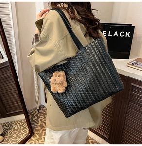 Detail of a black woven tote bag with a brown plush bear charm worn by a model