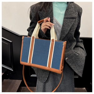 Detail van een denim tas met bruine lederen bies en witte banden voor dagelijks gebruik