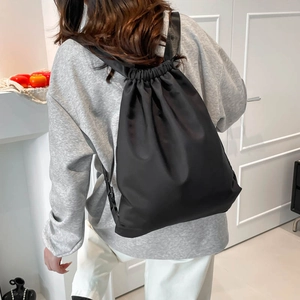 Minimalist black nylon drawstring backpack shown from a 45-degree back view for daily travel