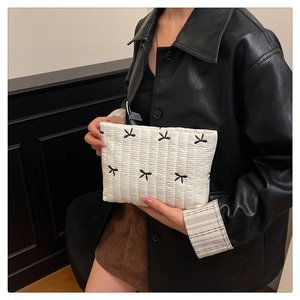 Dettaglio della pochette trapuntata bianca con ricamo di fiocchi neri tenuta da una modella