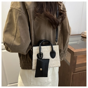 Detail view of woven straw tote bag with black leather trim and mini envelope pouch