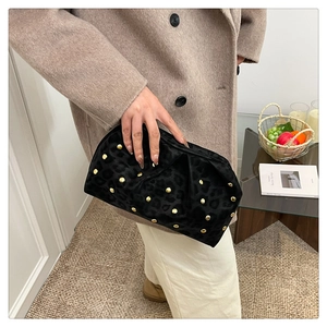 Detail of black leopard cloud clutch with gold studs held by a model in a modern room