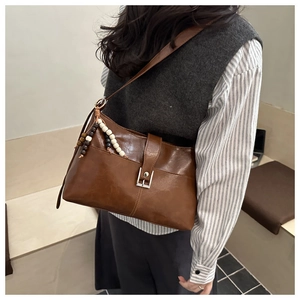 Close-up of brown vintage faux leather shoulder bag with silver buckle and bead charm
