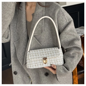 Detail of tweed shoulder bag with golden lock and white handle on wool coat background