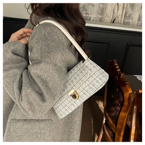 Close-up of elegant white tweed underarm bag with gold metal lock on a grey wool coat