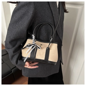 Detail of beige suede bucket bag with black leather trim and lace bow charm accessory