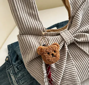 Detail of grey-blue corduroy handbag featuring a large bow and a brown plush bear charm