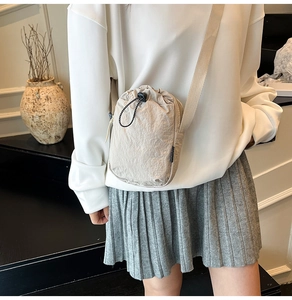 Detail of a beige nylon crossbody mini bag with drawstring closure and textured finish