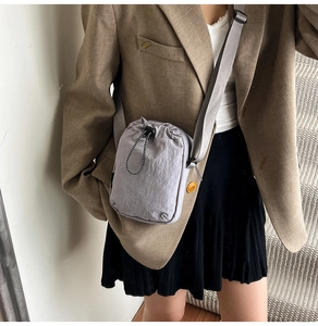 Detailed view of gray nylon crossbody bag with drawstring closure on model