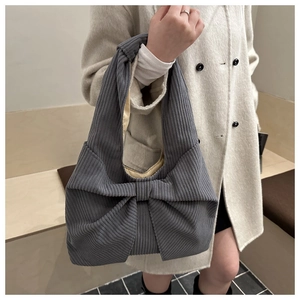Détail d'un sac à bandoulière en velours côtelé gris avec nœud sur un manteau blanc