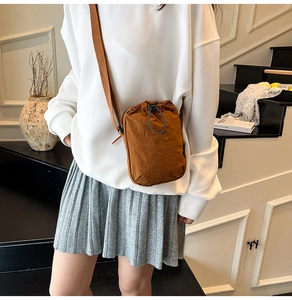 Brown nylon mini crossbody bag with drawstring closure worn by model in casual style