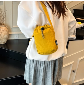 Close-up of ginger yellow nylon drawstring crossbody bag worn by a model in a cozy room