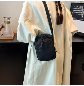 Detail of a black nylon mini crossbody water bottle bag with drawstring closure and strap