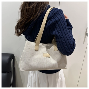 Detail of beige canvas tote bag with brown leather handles and decorative stitched label