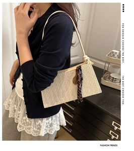Detail of woven straw shoulder bag featuring decorative fringe and knotted strap design