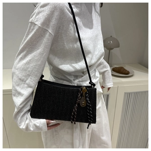 Detalle del bolso bandolera tejido negro con colgantes de raqueta de tenis y llave