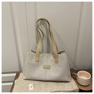 Detailed texture of beige linen tote bag with brown leather straps in a home setting