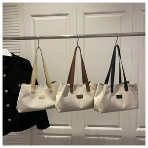 Three canvas tote bags in beige, brown, and black hanging on a metal display rack