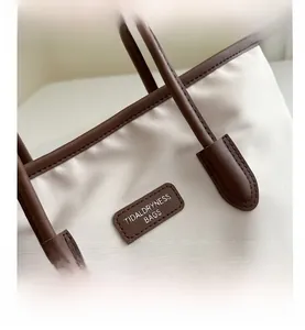 Detail view of canvas tote bag stitching with brown leather trim and brand logo tag