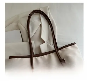 Detail of off-white tote bag with brown leather handles and brand label on fabric