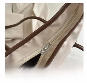 Detail of silver metal zipper closure on a beige nylon tote bag with brown leather trim