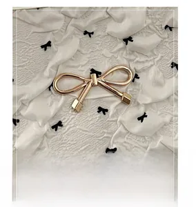 Détail de la décoration en forme de nœud en métal doré poli sur un sac à pois à la mode