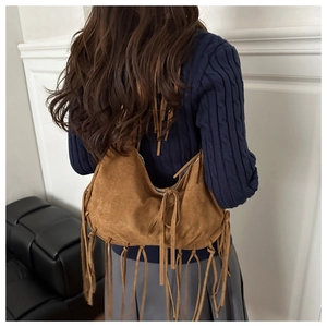 Detalle de bolso de hombro en ante marrón con flecos bohemios y forma de media luna