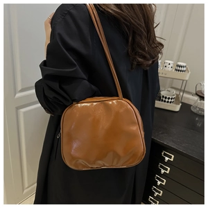 Detailed close-up of glossy brown faux leather shoulder bag with sleek metal zipper
