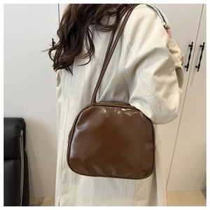 Detailed side view of a brown vintage oil wax leather shoulder bag on a beige coat model